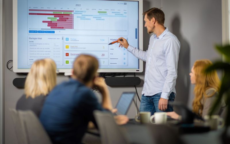 Foredragsholder som viser en graf på en skjerm i forbindelse med miljørapportering.