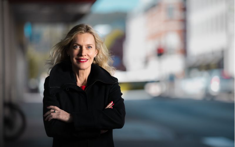 Dame med armene i kors poserer med bybakgrunn