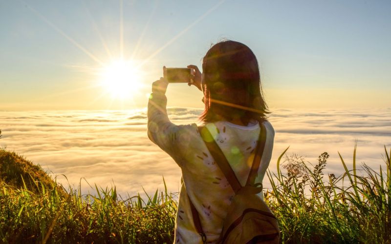 Person som tar mobilfoto av en solnedgang fra et fjell.