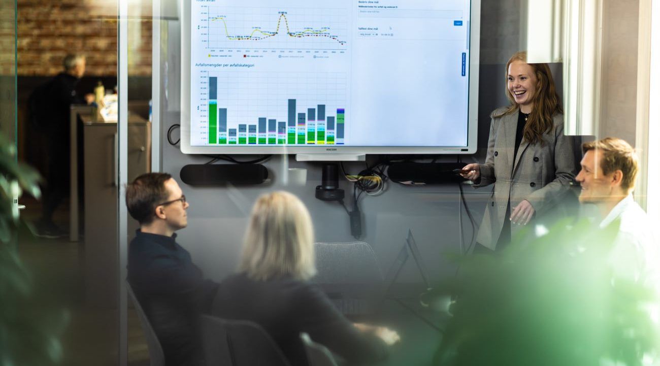 Bilde av en gruppe mennesker i møterom som ser på stor statistikkdata på skjerm