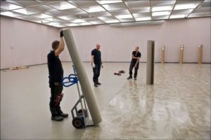 Tre menn som jobber med gulvbelegg i lokale