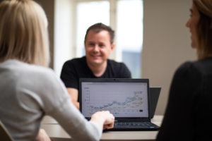 Tre personer sitter i møte med laptop med skjermbilde av en graf