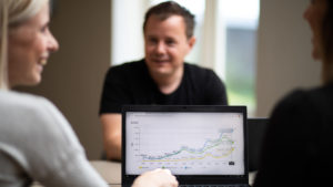 En mann og to damer prater sammen i møte med laptop