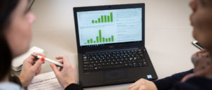 To damer som snakker og ser på en laptop med grafer