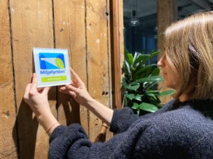 Bilde av dame som henger opp Miljøfyrtårn-skilt