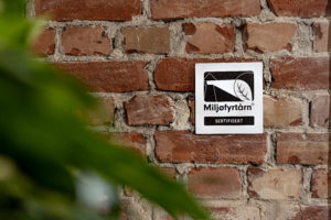 Bilde sort-hvit Miljøfyrtårn-aluminiumsplakett hengende på murvegg