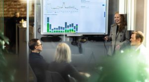 Bilde av en gruppe mennesker i møterom som ser på stor statistikkdata på skjerm