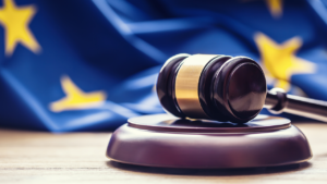 Bilde av en lov-hammer på et bord, og med et EU-flagg i bakgrunnen