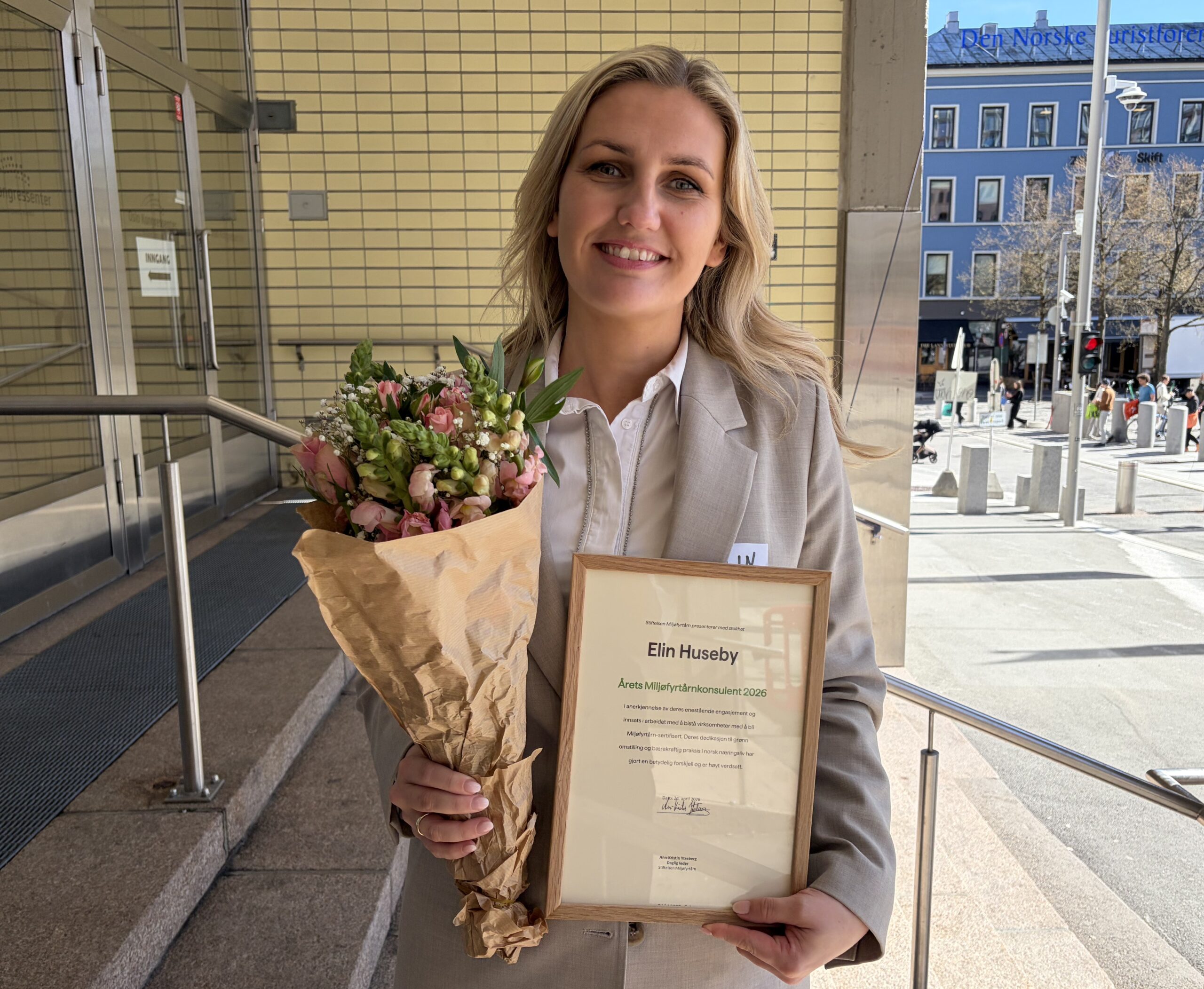 Kvinne som smiler til kamera. I hendene holder hun blomster og et diplom for Årets Miljøfyrtårn-konsulent 2026