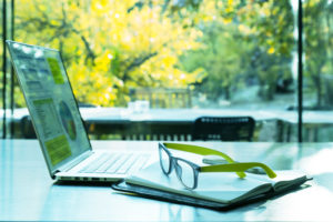 Bilde av laptop og briller med utsikt av trær i bakgrunnen