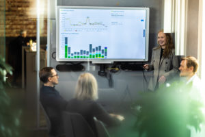 Bilde av en gruppe mennesker i møterom som ser på stor statistikkdata på skjerm