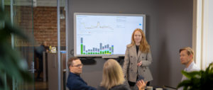Bilde av en gruppe mennesker rundt et møtebord med presentasjon av statistikk på skjerm