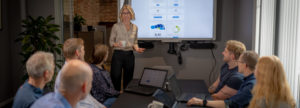Bilde av en gruppe mennesker rundt et møtebord med presentasjon på skjerm