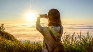 Person som tar mobilfoto av en solnedgang fra et fjell.